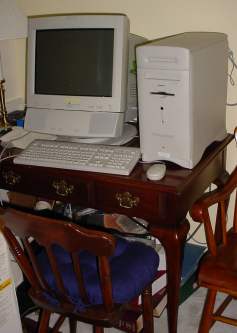 A Macintosh Performa sits on a small desk surrounded by nice old wooden chairs.