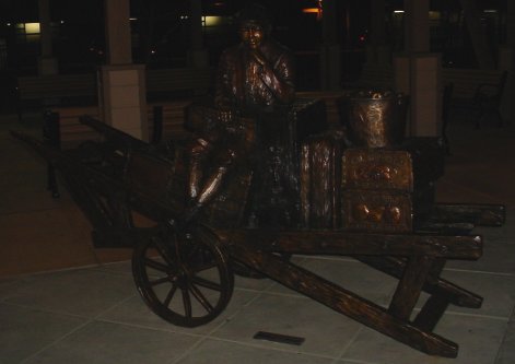 Bronze kid sits on a bronze luggage cart with bronze fruit from MountainView.