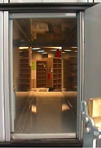 The inside of a well lit mailroom as seen through an open mailbox.