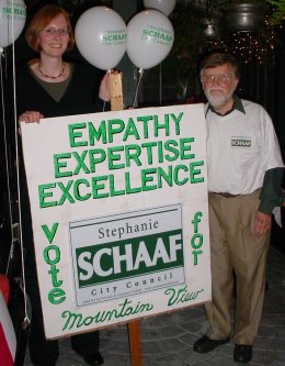 Stephanie stands behind a sign that says "Empathy, Expertise, Excellence Vote for Stephanei" with Fred to her right.