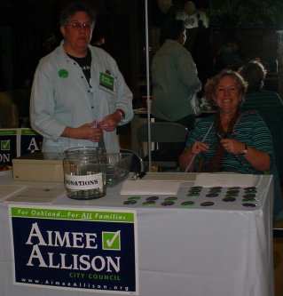 Two women sit at a table covered with Aimee Allison buttons and literature.