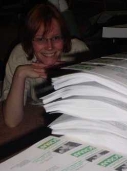 Stephanie smiles from behind a pile of newsletters.