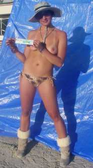 Woman in brown bikini bottom, sunglasses and shade hat poses in front of a blue tarp with a MEND YOUR FEULISH WAYS sticker.