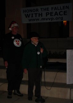 Two guys in front of a banner that says HONOR THE FALLEN WITH PEACE.