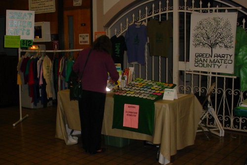 A table with lots of buttons on it sits between a rack of shirts and a GPSMC sign.