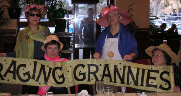 Raging Grannies pose with their banner.