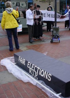 Fair Elections Coffin with speakers in background.