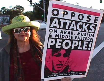 Dana stands with a sign that says OPPOSE ATTACKS on other PEOPLE.