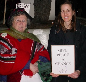 Two women sitting. One has a sign that says "GIVE PEACE A CHANCE".