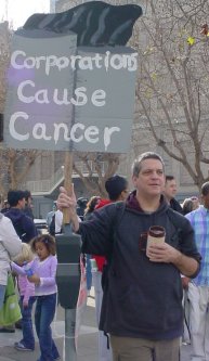 Guy with a sign that says "CORPORATIONS CAUSE CANCER".