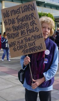 A woman holds a sign explaining that we need to learn how to live together.