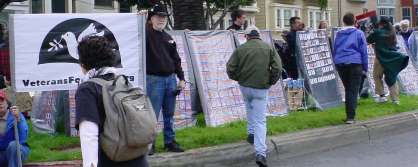 Veterans for Peace with a wall of pictures of their fallen bretheren.