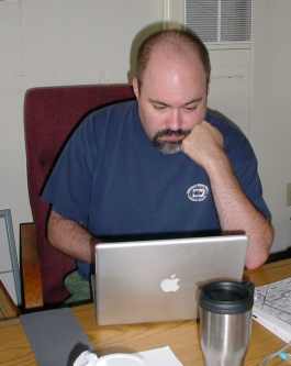 Jeff sits and ponders something on the screen of a Macintosh laptop computer.