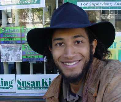 Julian Davis, in a black hat, poses by his campaign literature with a big smile.