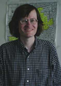 Tom smiles with a precinct map of District 5. Many precincts have yellow blotches on them.