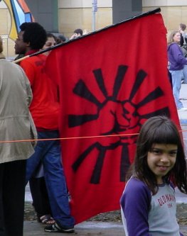 A young girl smiles and a guy with a power fist in the air on a flag walks away.