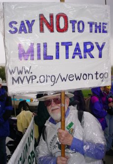 Fred carrying a saran wrapped sign that says "SAY NO TO THE MILITARY".