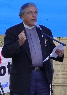 Man in a priest's colar talks at the mike.
