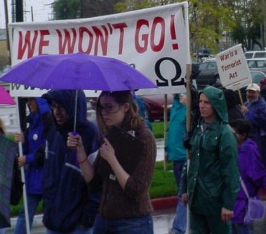 Banner that says "WE WONT GO!" with an omega. Other words are hidden behind a purple umbrella.