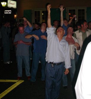 People stand with arms raised as if saying "throw them here". One person has shirt open showing breasts.