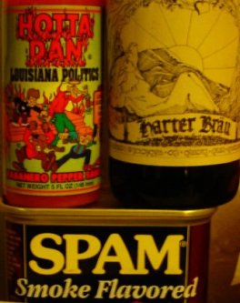 A bottle of hot sauce sits on a can of SPAM.