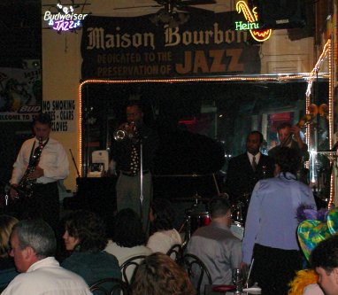 Jazz band plays behind audience seated at tables.