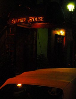 Dark street. The words QUARTER HOUSE  are visible in the awning over a door.